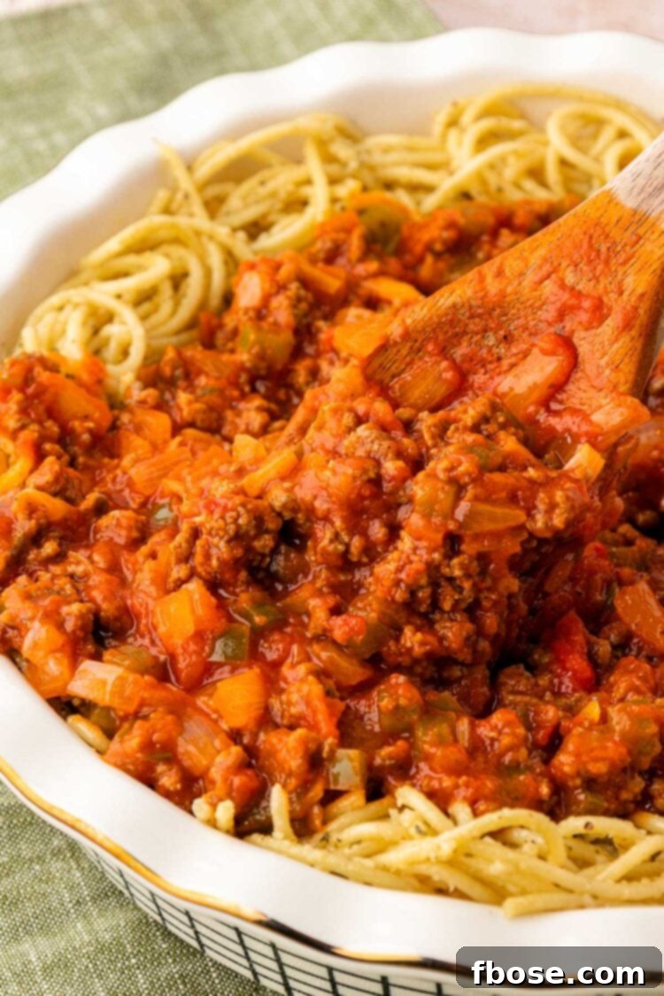 Bolognese Sauce being added to the center of a pie dish filled with spaghetti.