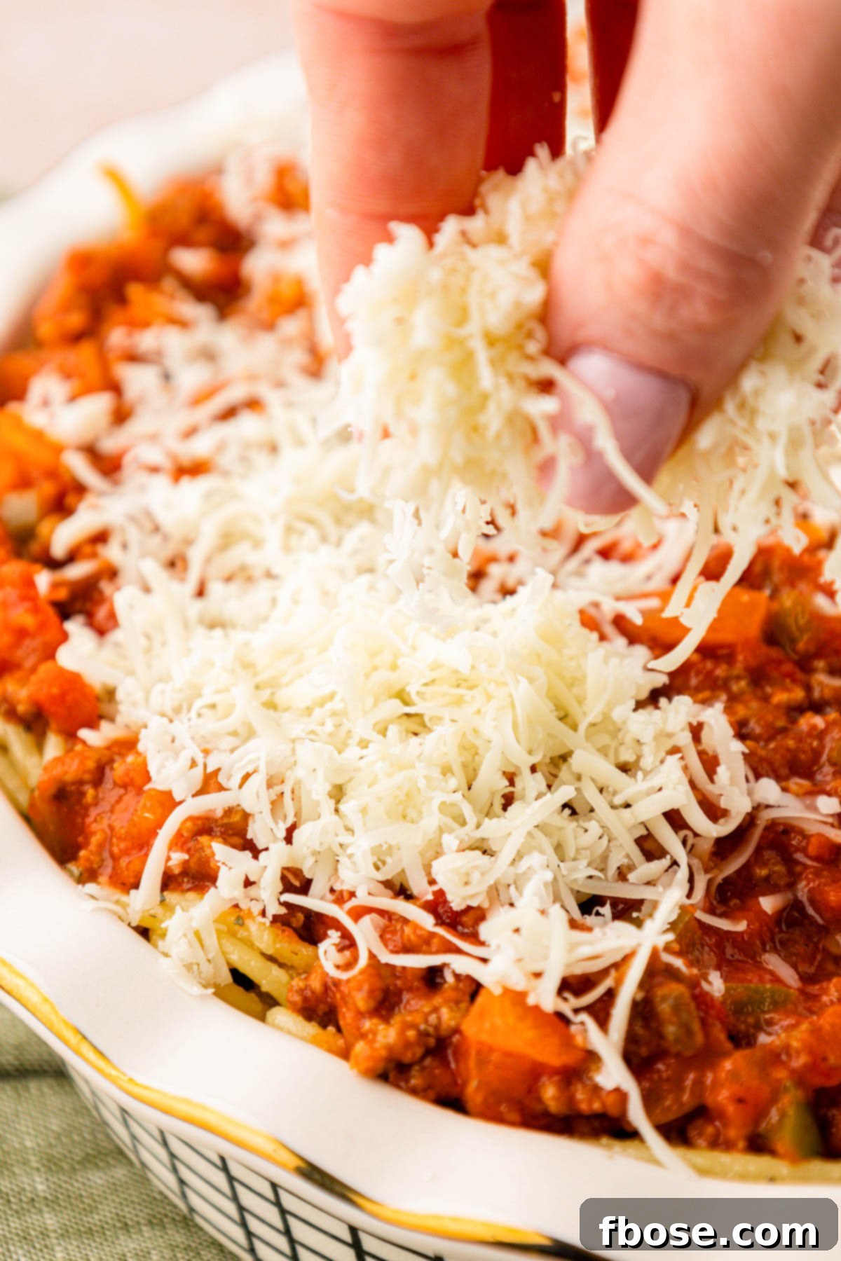 Shredded mozzarella being added to a spaghetti pie.
