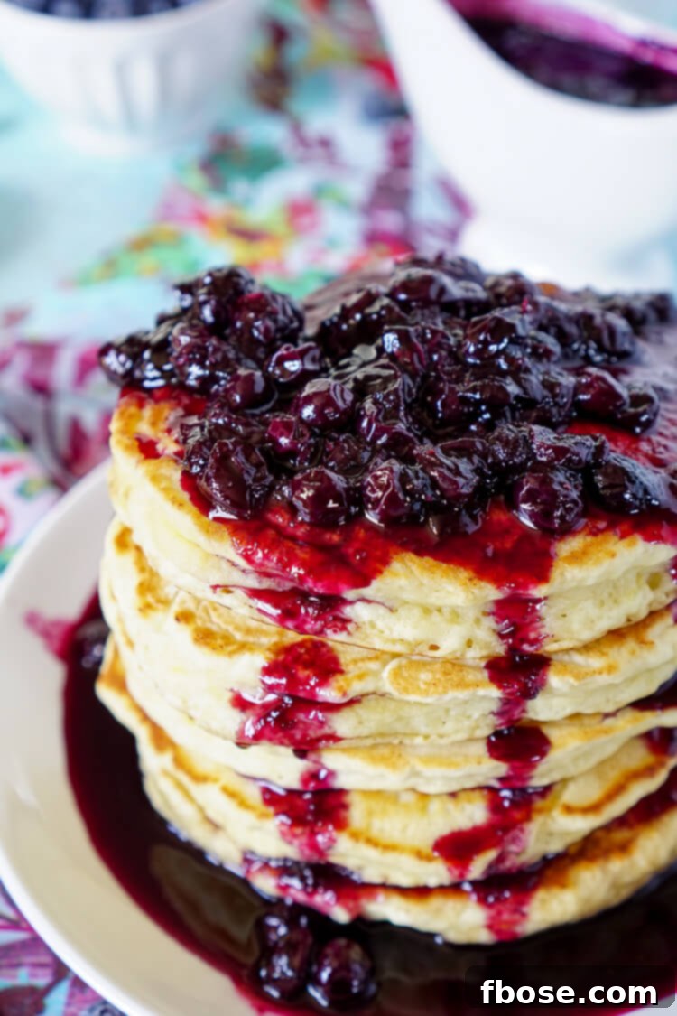 Close-up of fluffy Lemon Ricotta Pancakes stacked high, drizzled with vibrant blueberry compote.