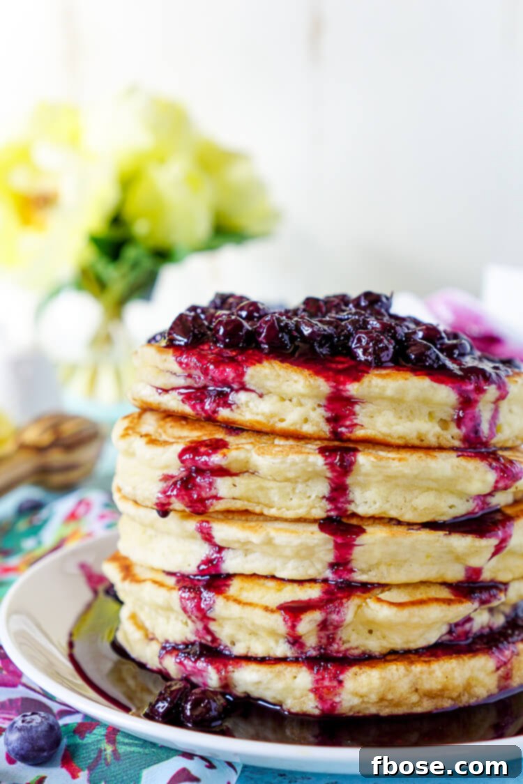 Golden brown Lemon Ricotta Pancakes topped with rich, warm blueberry compote and a sprig of mint.