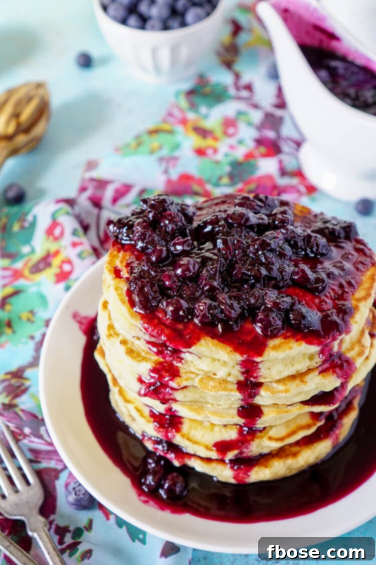 A stack of light and airy Lemon Ricotta Pancakes on a plate, generously covered with sweet blueberry compote.