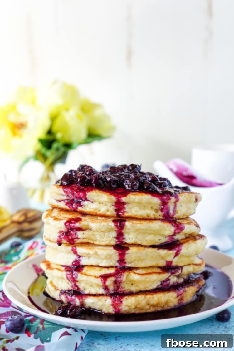Overhead shot of two Lemon Ricotta Pancakes, bursting with lemon zest and ricotta, adorned with fresh blueberries and compote.
