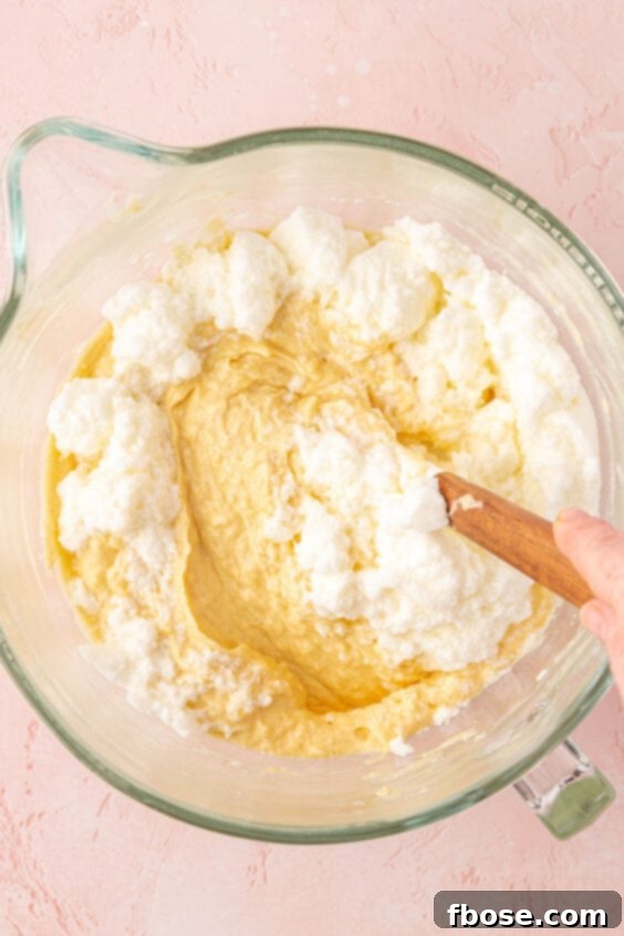 Stiff egg whites being folded into coconut cake batter.