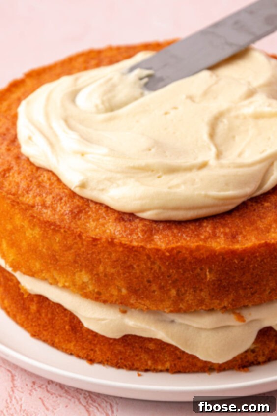 Two layers of yellow coconut cake being frosted on a plate.