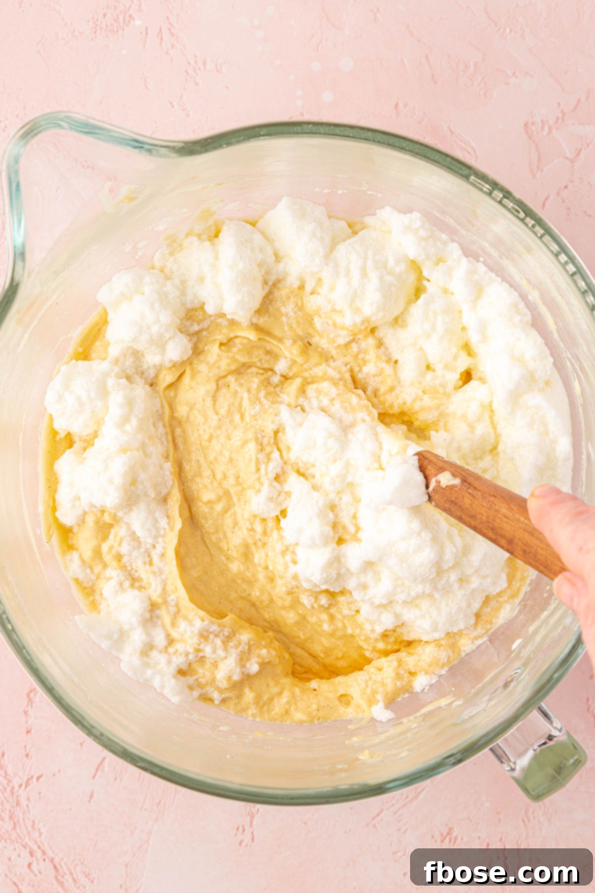 Delicately folding whipped egg whites into the light coconut cake batter, a key step for achieving a fluffy texture.