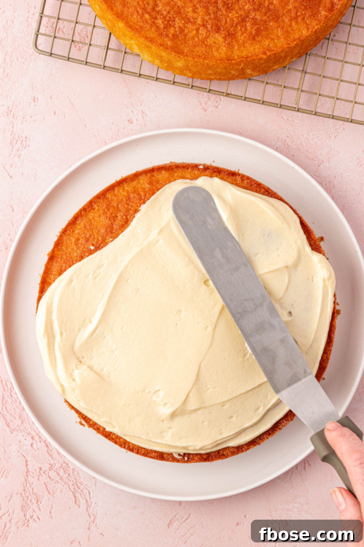 An offset spatula expertly applies creamy frosting to a freshly baked cake layer, a key step in creating the Classic Coconut Cake.