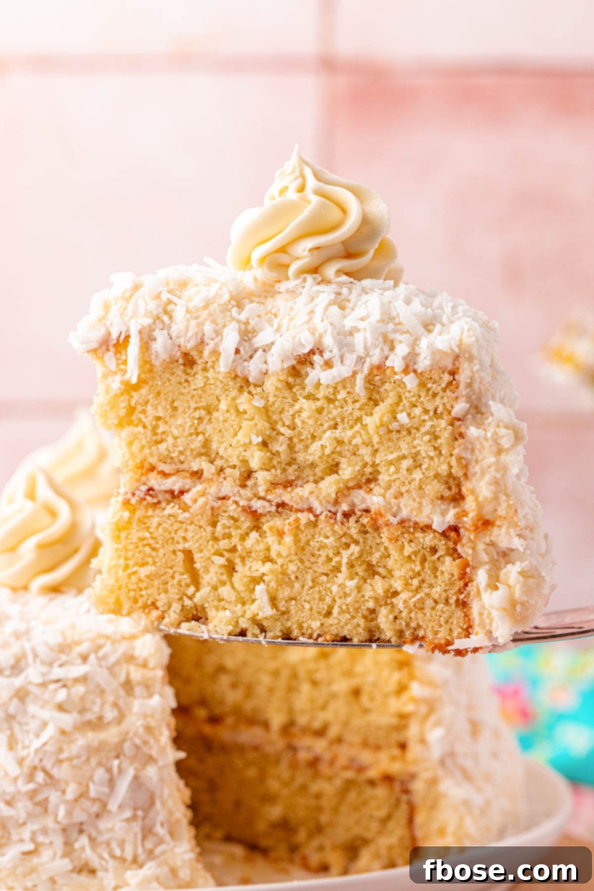 A delicate slice of moist yellow coconut cake being lifted away from the main cake, revealing its beautiful layers and frosting.