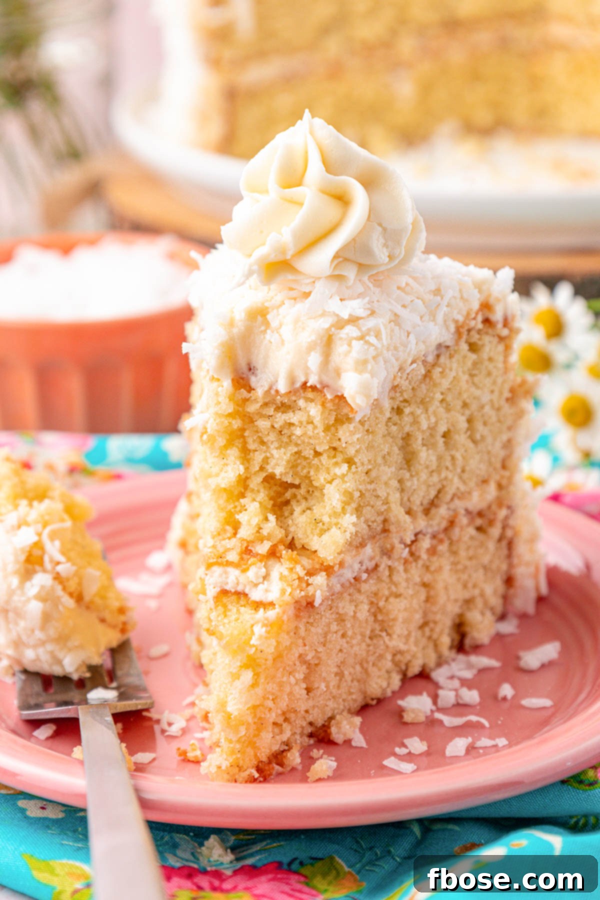 A delicious slice of coconut cake with a bite taken out, resting on a pink plate, inviting another taste.