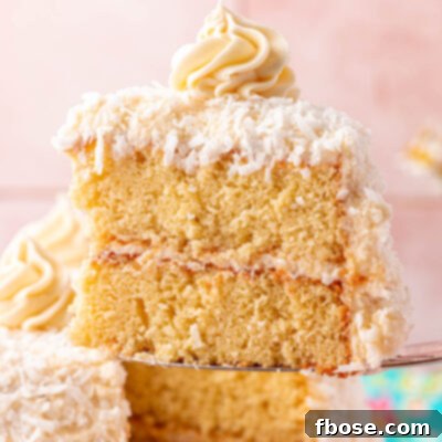 A slice of yellow coconut cake being lifted away from the whole cake.