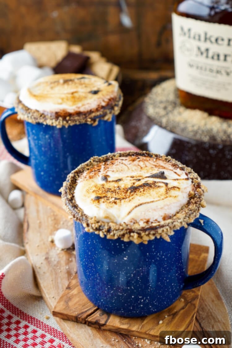 A Campfire S'mores Hot Chocolate Cocktail garnished with a chocolate-dipped, graham-crusted rim and perfectly toasted marshmallow fluff.