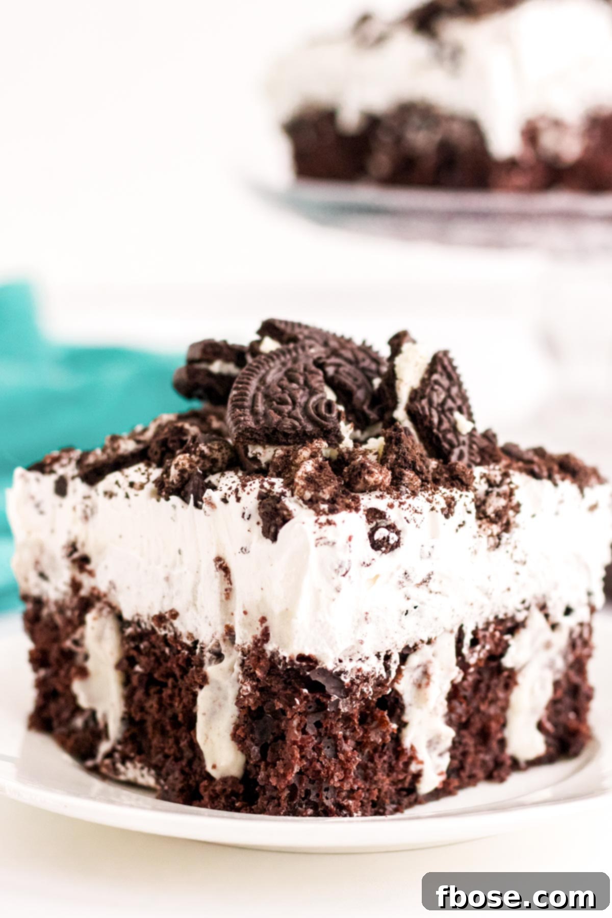 Close up photo of a slice of Oreo poke cake on a white plate, highlighting the delicious textures.