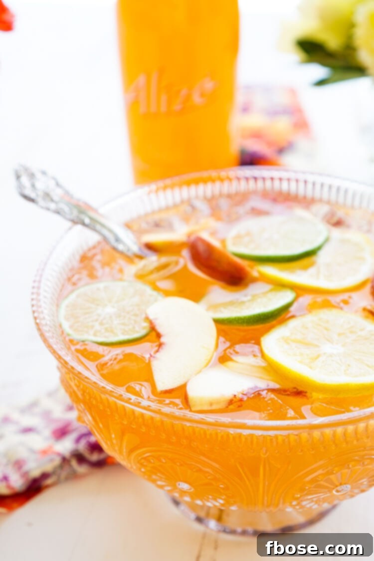 A large glass pitcher filled with vibrant Spiked Peach Punch, garnished with fresh peach slices, lime, and mint, perfect for summer gatherings.