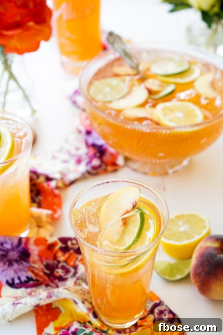 A vibrant close-up of the Spiked Peach Punch in a clear glass pitcher, with fresh peaches and lime slices, ready for a party.