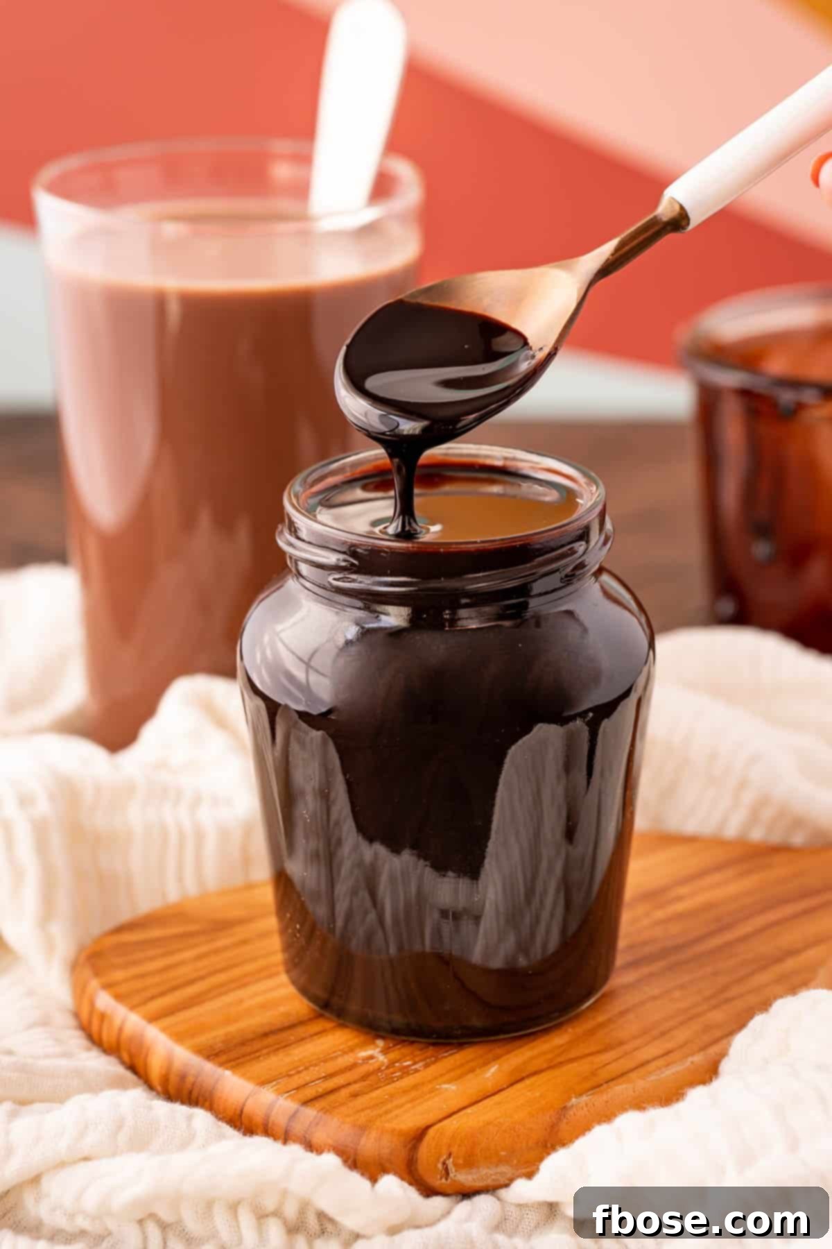 Homemade chocolate syrup in a glass jar, with a white spoon resting inside, ready to be served.