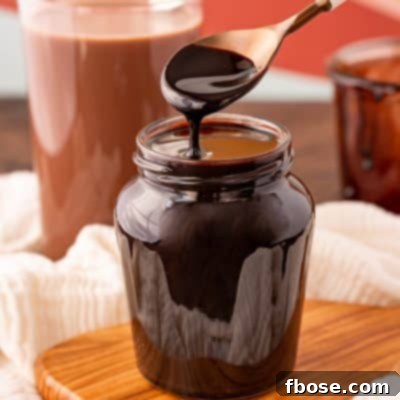 Chocolate syrup in a jar with a white spoon.