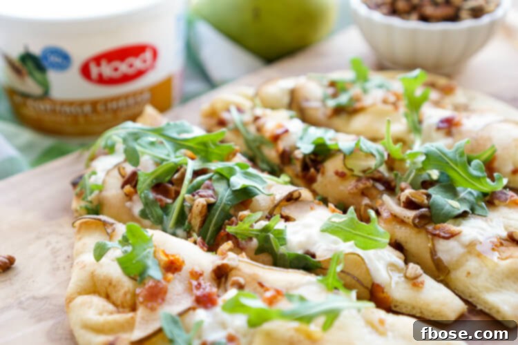 Hand holding a slice of Honey Pear Bacon Flatbread, displaying the melted cottage cheese, crispy bacon, and fresh arugula, highlighting its delectable appeal.