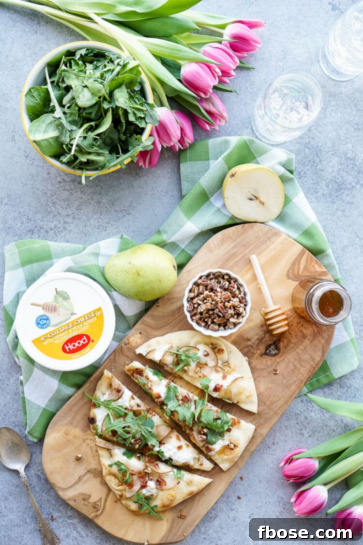 A rustic cutting board featuring a freshly baked Honey Pear Bacon Flatbread, garnished with vibrant green arugula and a generous drizzle of honey.