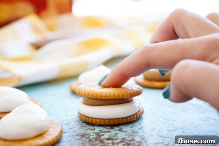 Hands preparing Fluffernutter RITZwiches, showing the process of spreading peanut butter and marshmallow fluff on RITZ crackers. Emphasizes the quick 5-minute preparation time.