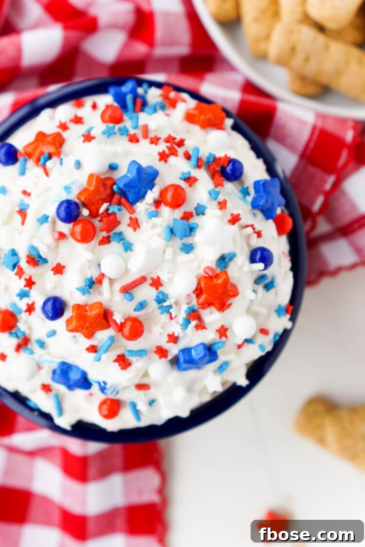Red, White and Blue Cake Batter Dip 4 Overhead view of a beautifully presented Cake Batter Dip in a white bowl, surrounded by an assortment of dippers like vanilla wafers, pretzels, and fresh strawberries.