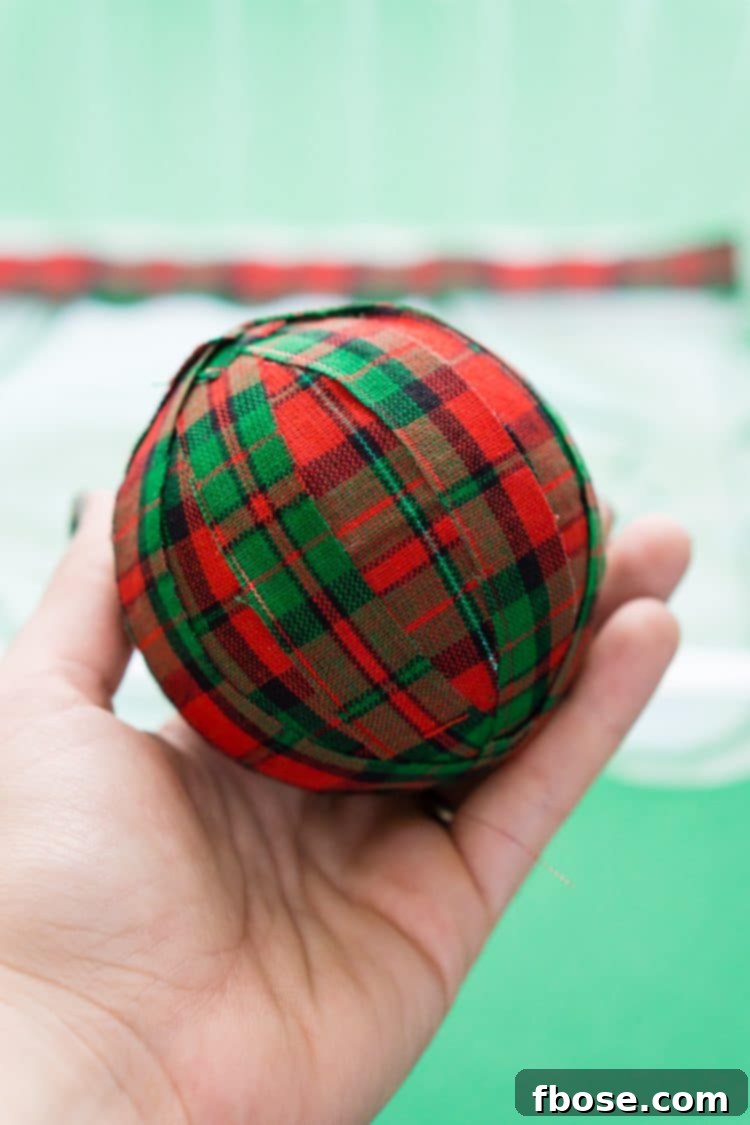 Completing the DIY Holiday Rag Ball by continuously wrapping fabric strips until fully covered.