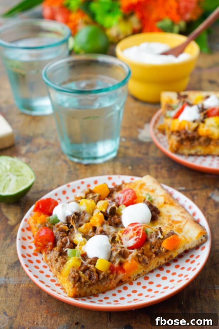 Close-up of a delicious Taco Pizza slice with a crispy crust, seasoned beef, melted cheese, and fresh toppings, ready to be enjoyed.