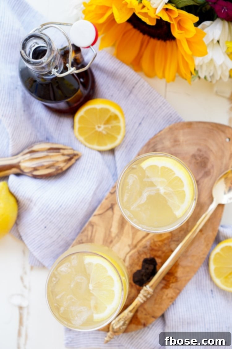 Close-up of Maple Lemonade in a clear glass, showing ice cubes, lemon slices, and the golden hue of the drink.