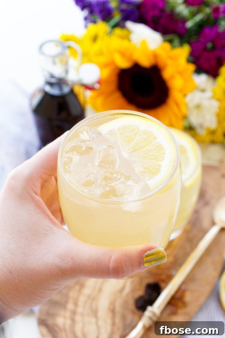 A close-up shot of Maple Lemonade, with water being poured into a glass filled with lemon slices and maple syrup.