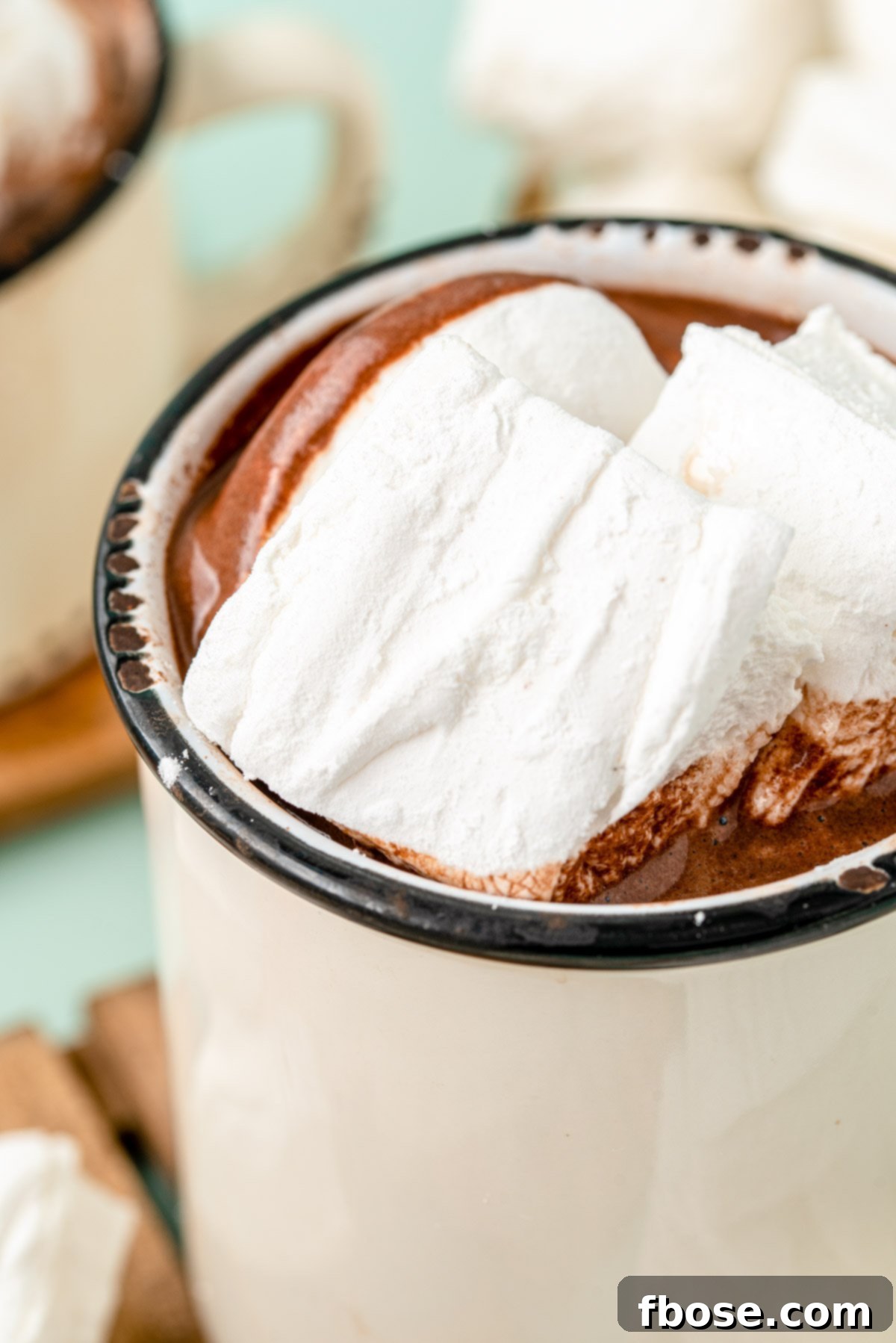 Homemade marshmallows in a white mug filled with hot chocolate. The mug sits on a wooden surface beside a festive green napkin.