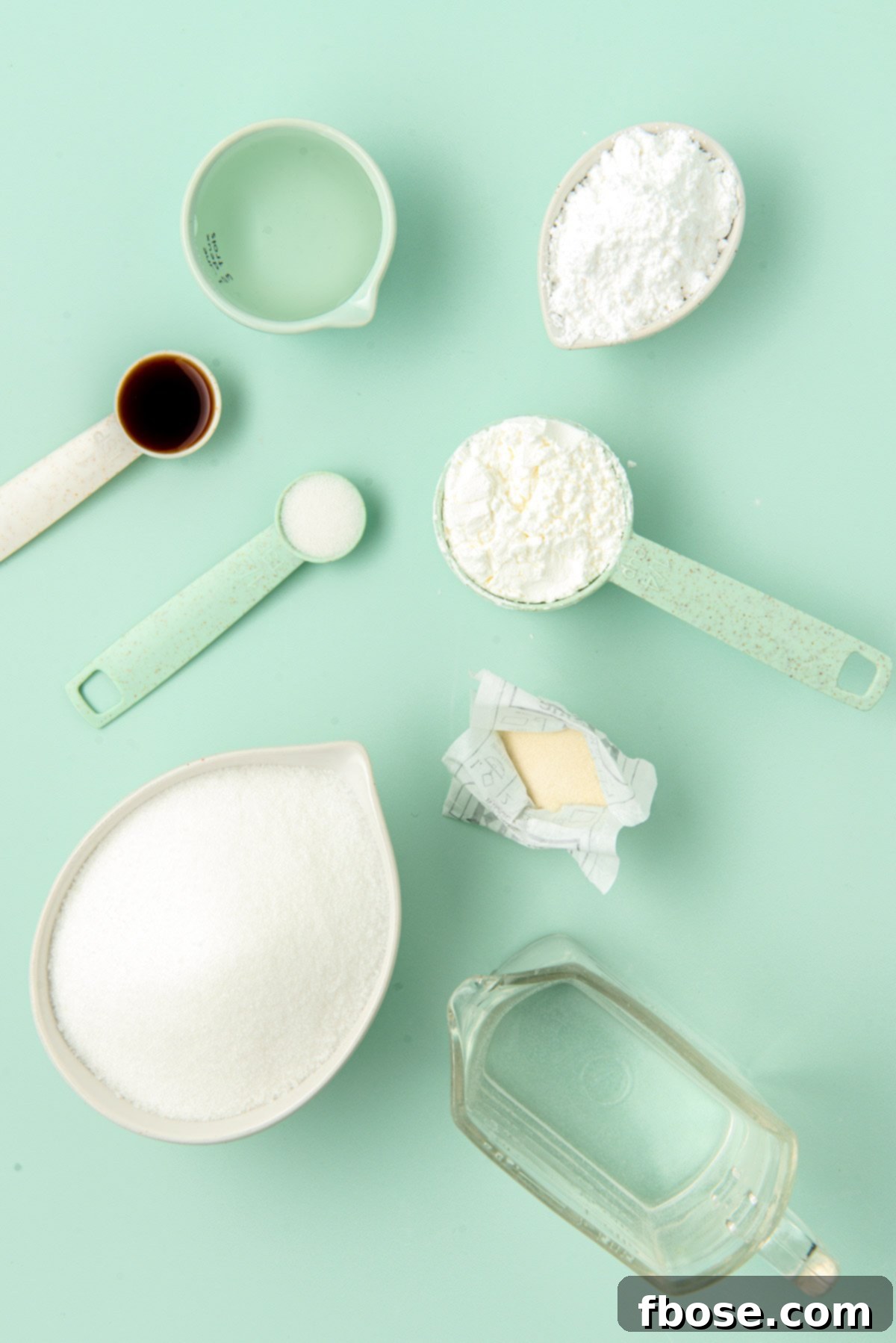 Ingredients to make homemade marshmallows laid out on a vibrant green table, including sugar, gelatin, corn syrup, and vanilla extract.