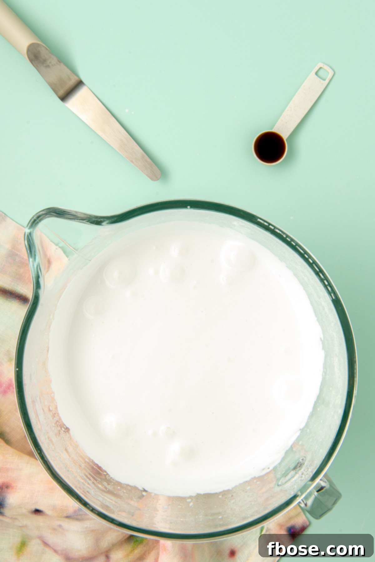 Thick, fluffy, and glossy marshmallow cream being whipped in a glass mixing bowl by a stand mixer.