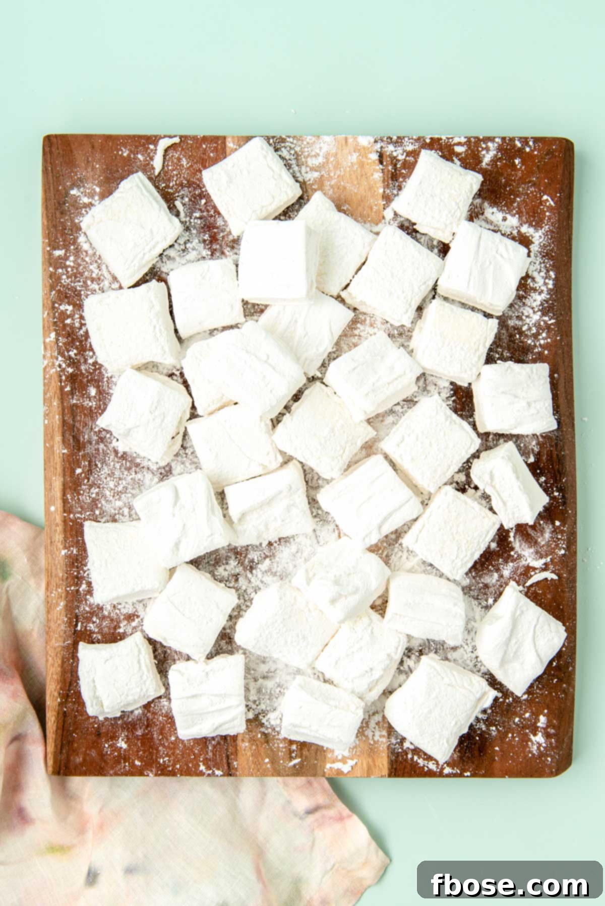 Perfectly cubed homemade marshmallows dusted with powdered sugar and arranged on a wooden cutting board.