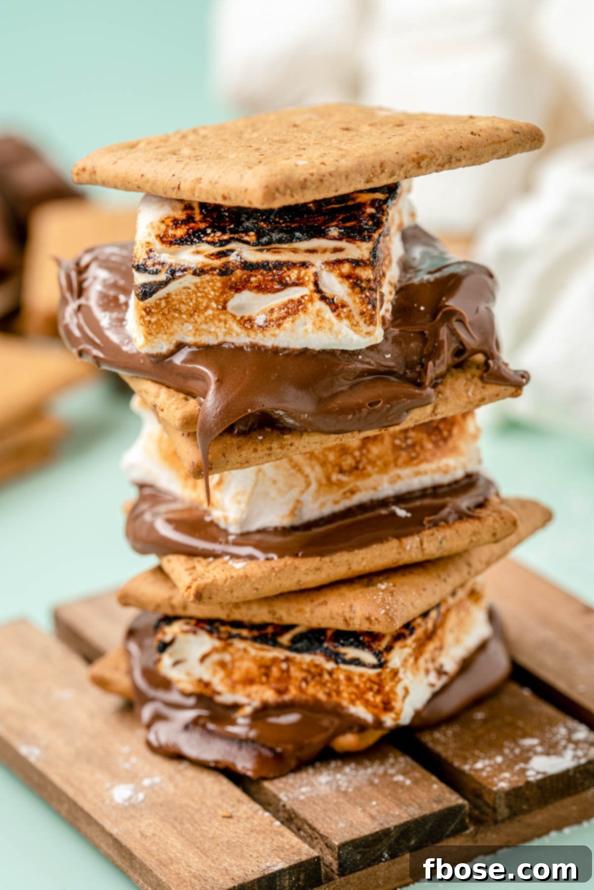 Delicious s'mores made with golden-brown homemade marshmallows, chocolate, and graham crackers stacked on a wooden coaster.