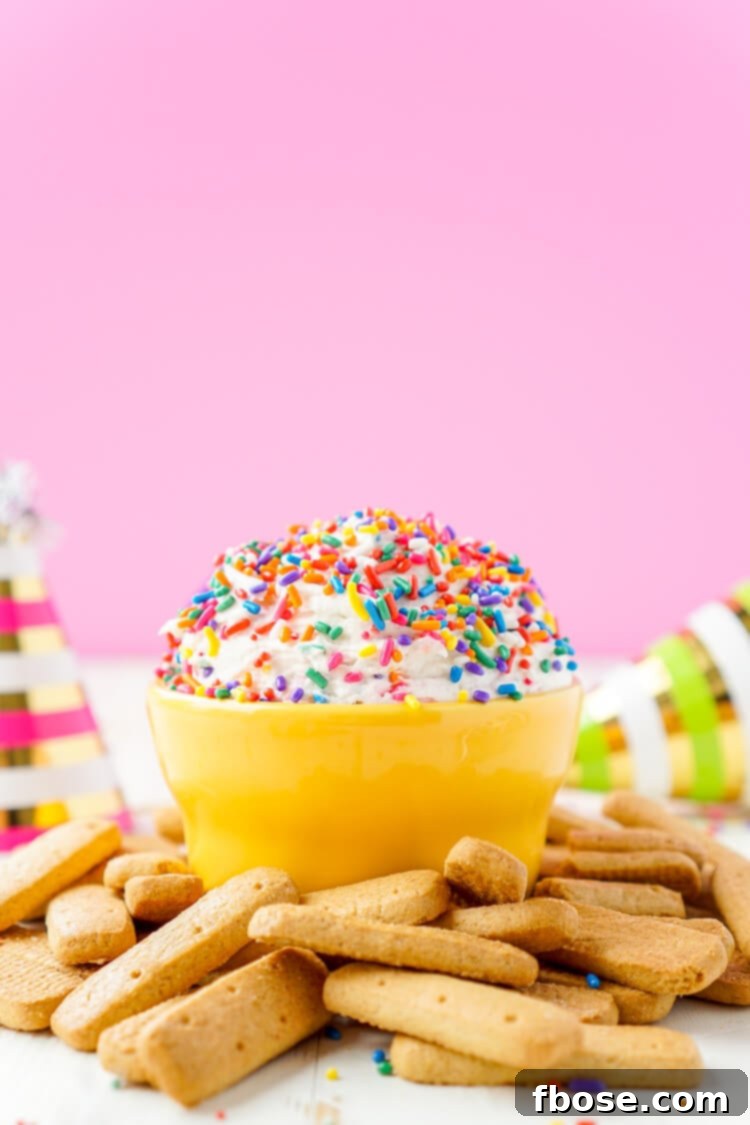 Overhead shot of the Funfetti Birthday Cake Dip in a glass bowl, surrounded by various dippers like cookies.