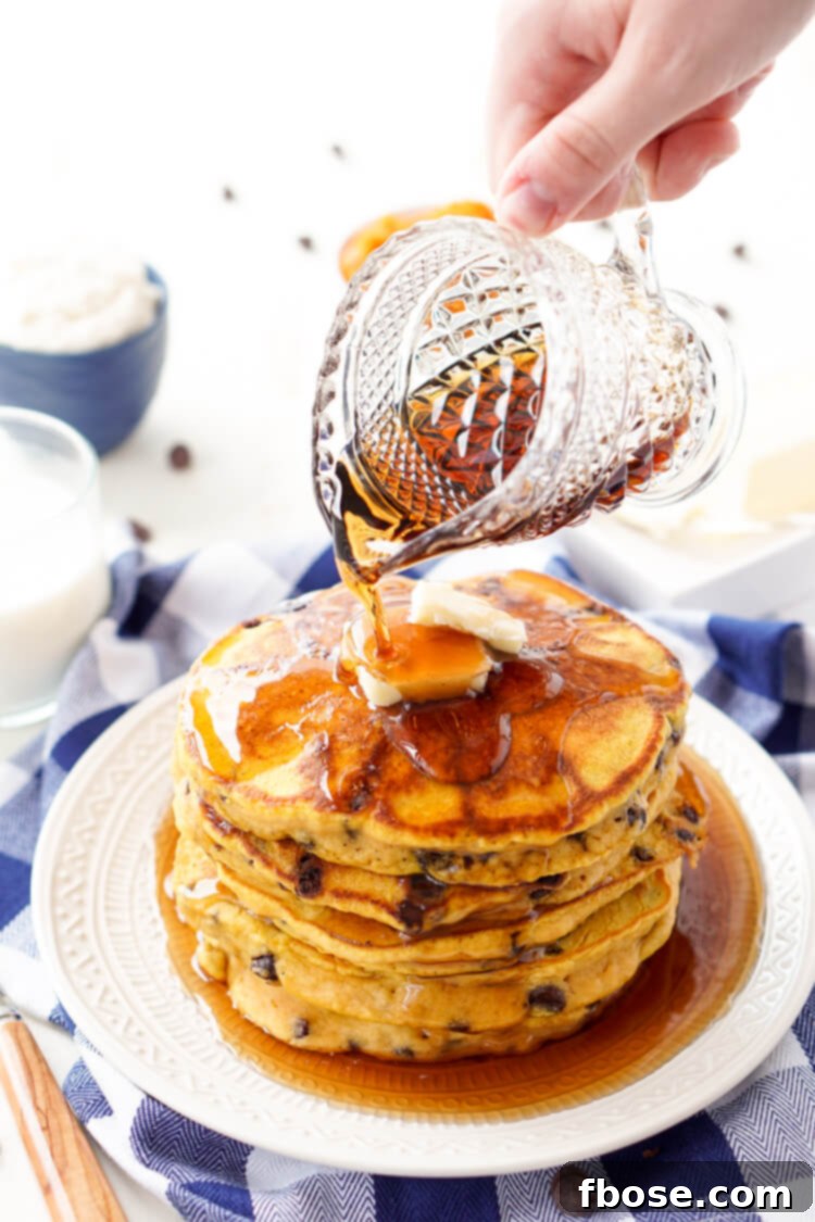 Fluffy Pumpkin Chocolate Chip Pancakes stacked high, drizzled with maple syrup and melting butter, perfect for a cozy fall breakfast.