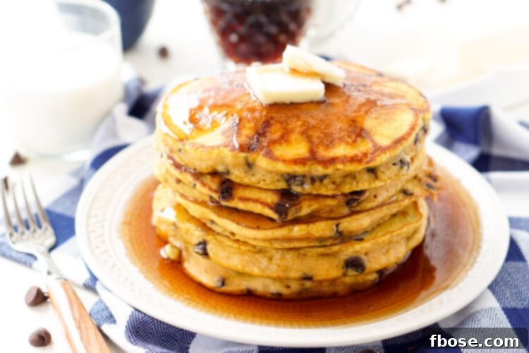 A towering stack of Pumpkin Chocolate Chip Pancakes, generously topped with whipped cream, butter, and maple syrup, ready for a delicious breakfast.