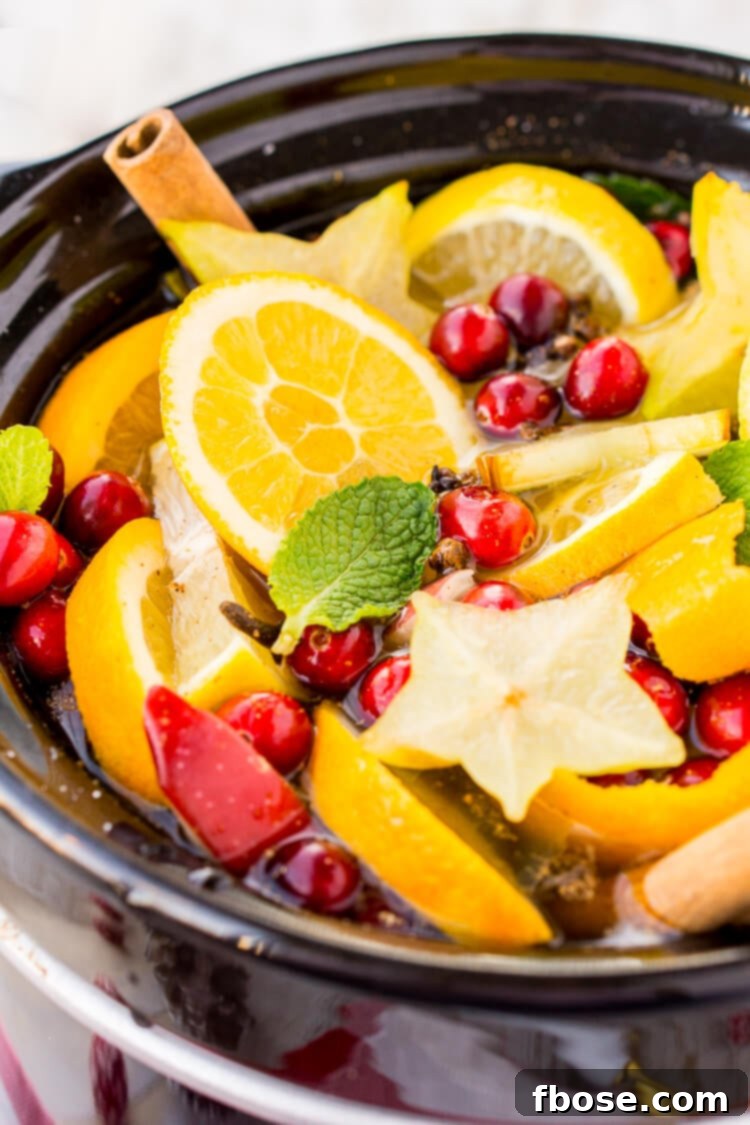 A festive spread of ingredients for DIY Holiday Crock Pot Potpourri, including cranberries, oranges, mint, cloves, and cinnamon sticks.