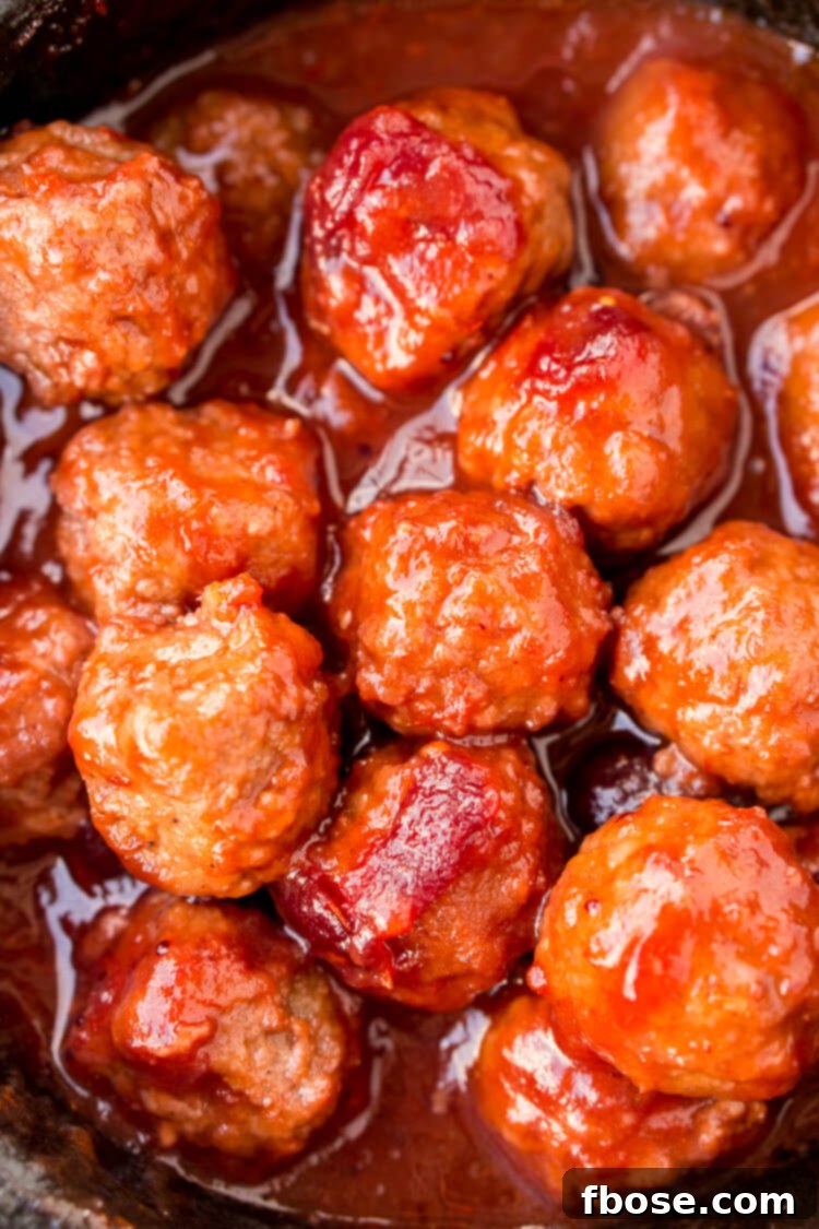Overhead shot of Cranberry Orange Meatballs in a crockpot, garnished with fresh rosemary and orange slices, ready for serving.