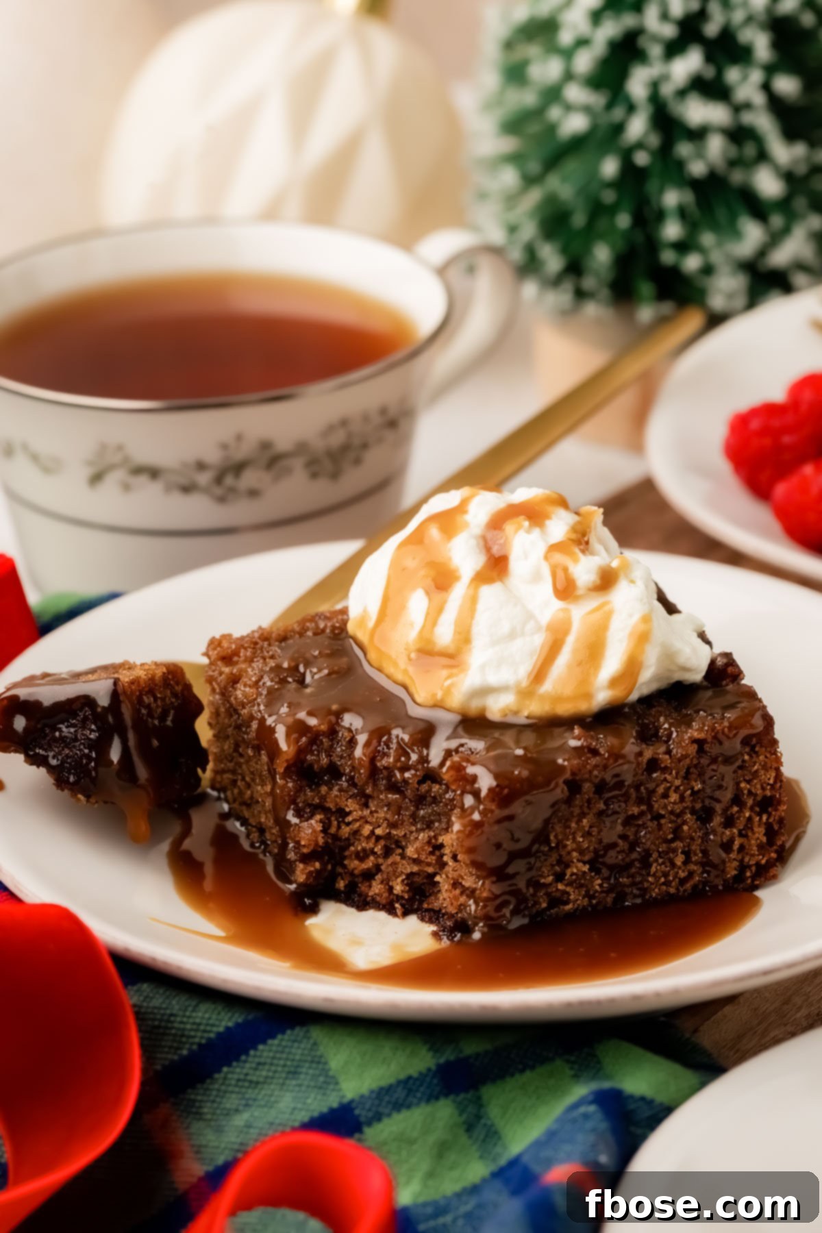 A slice of sticky toffee pudding on a white plate with a bite taken out of it.