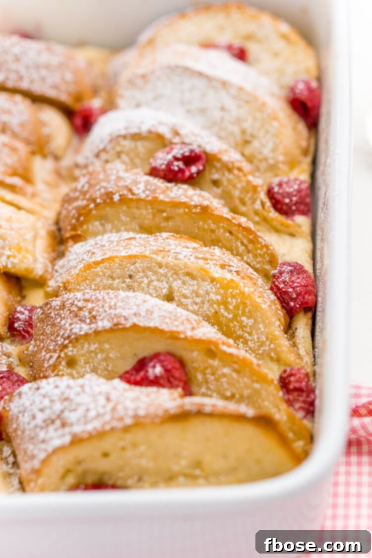 Golden-brown Champagne Raspberry Baked French Toast slices served with fresh raspberries, a dusting of powdered sugar, and a drizzle of maple syrup for a festive breakfast.