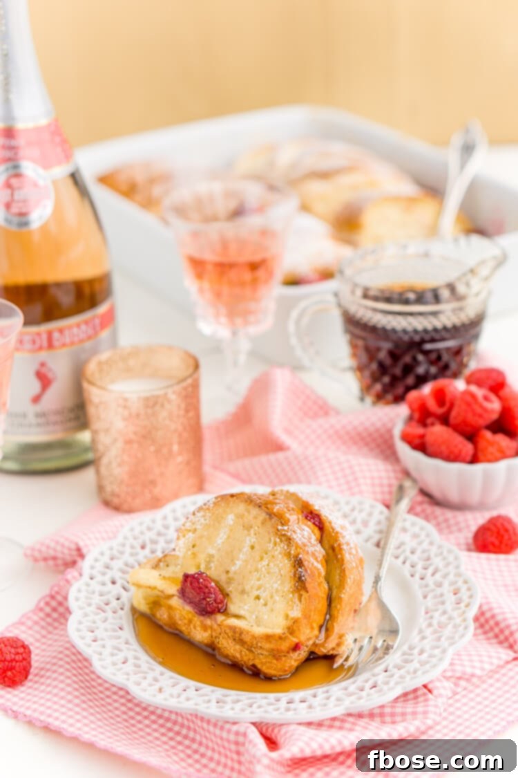 Delicious Champagne Raspberry Baked French Toast garnished with a light sprinkle of confectioners' sugar and whole raspberries, ready for a special occasion.