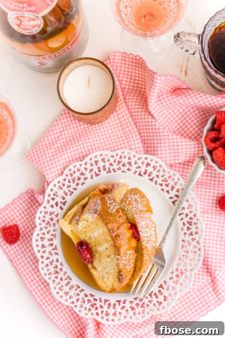 Overhead view of a beautiful Champagne Raspberry Baked French Toast casserole in a baking dish, adorned with fresh raspberries, ready to be served.