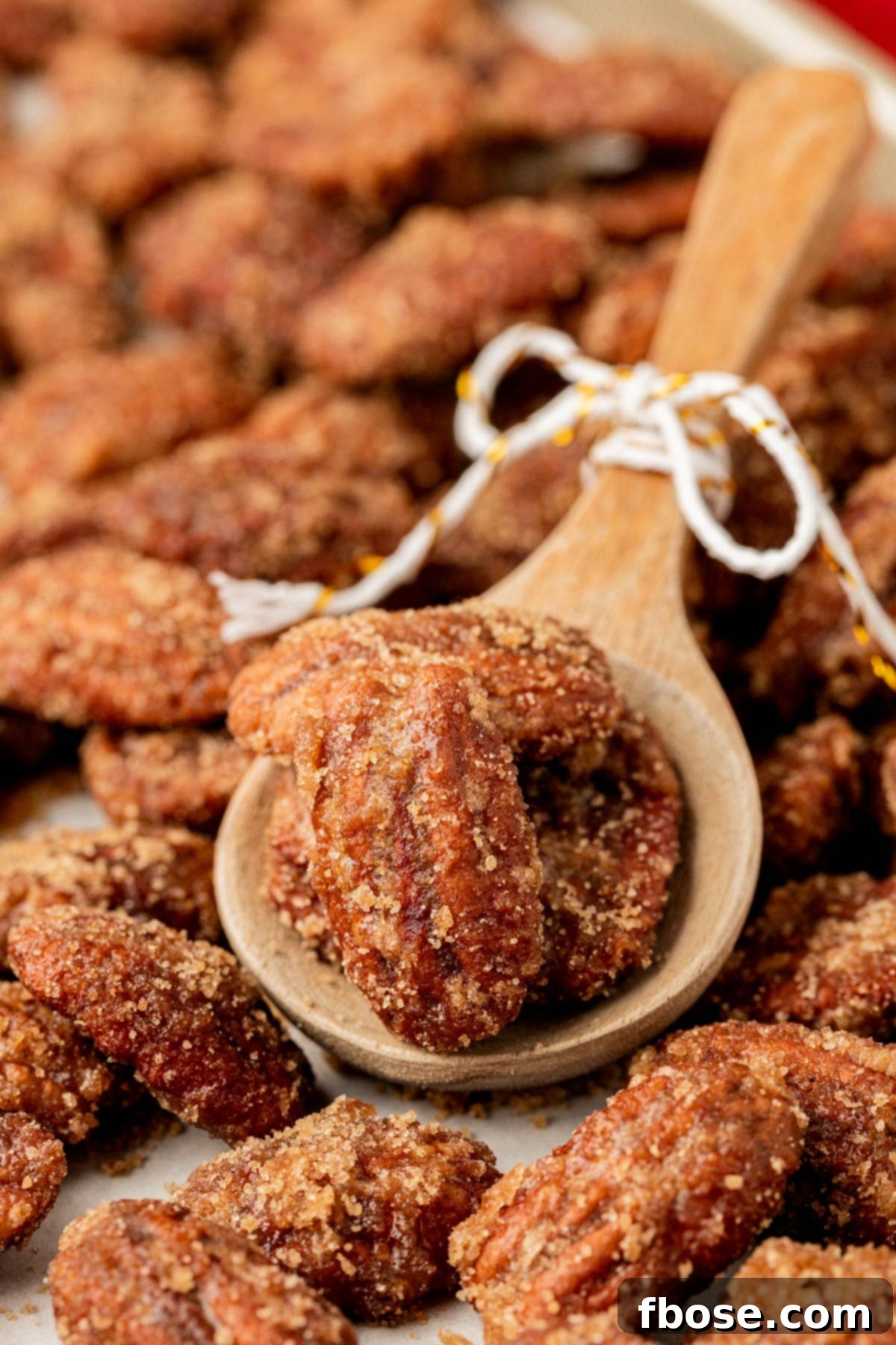 A wooden spoon carefully scooping caramelized pecans from a skillet, showing their glossy coating.