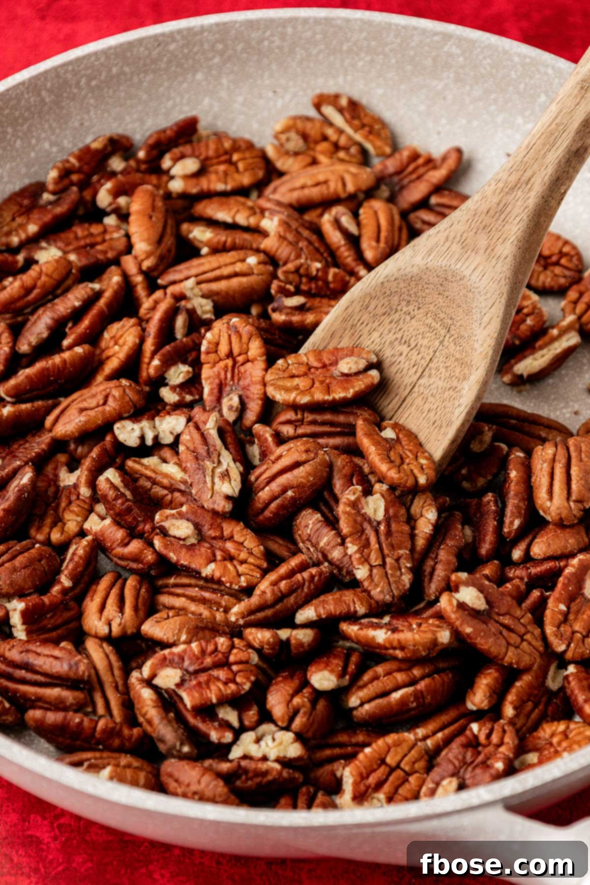 Pecan halves being gently toasted in a large, nonstick skillet on the stovetop, releasing their nutty aroma.