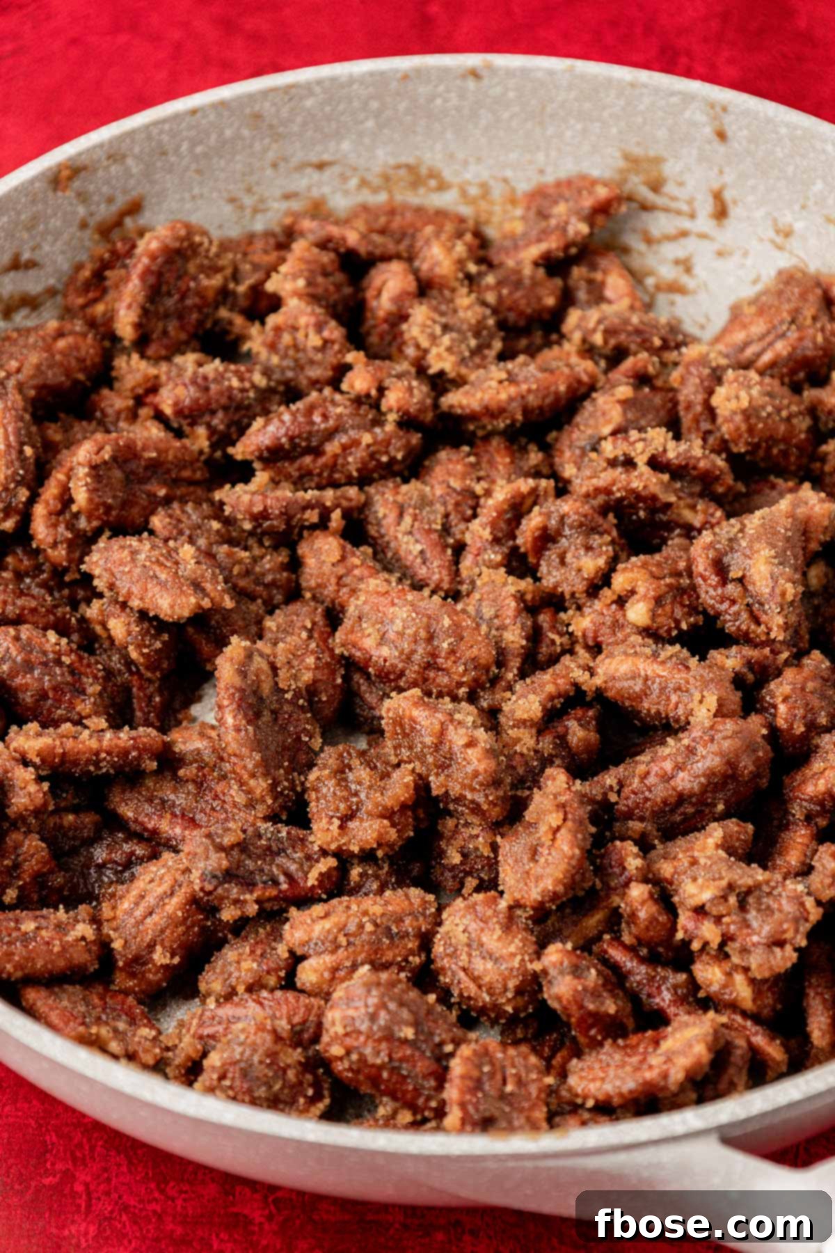 Freshly candied pecans in a nonstick skillet, glistening with a sugary coating, ready to be transferred.