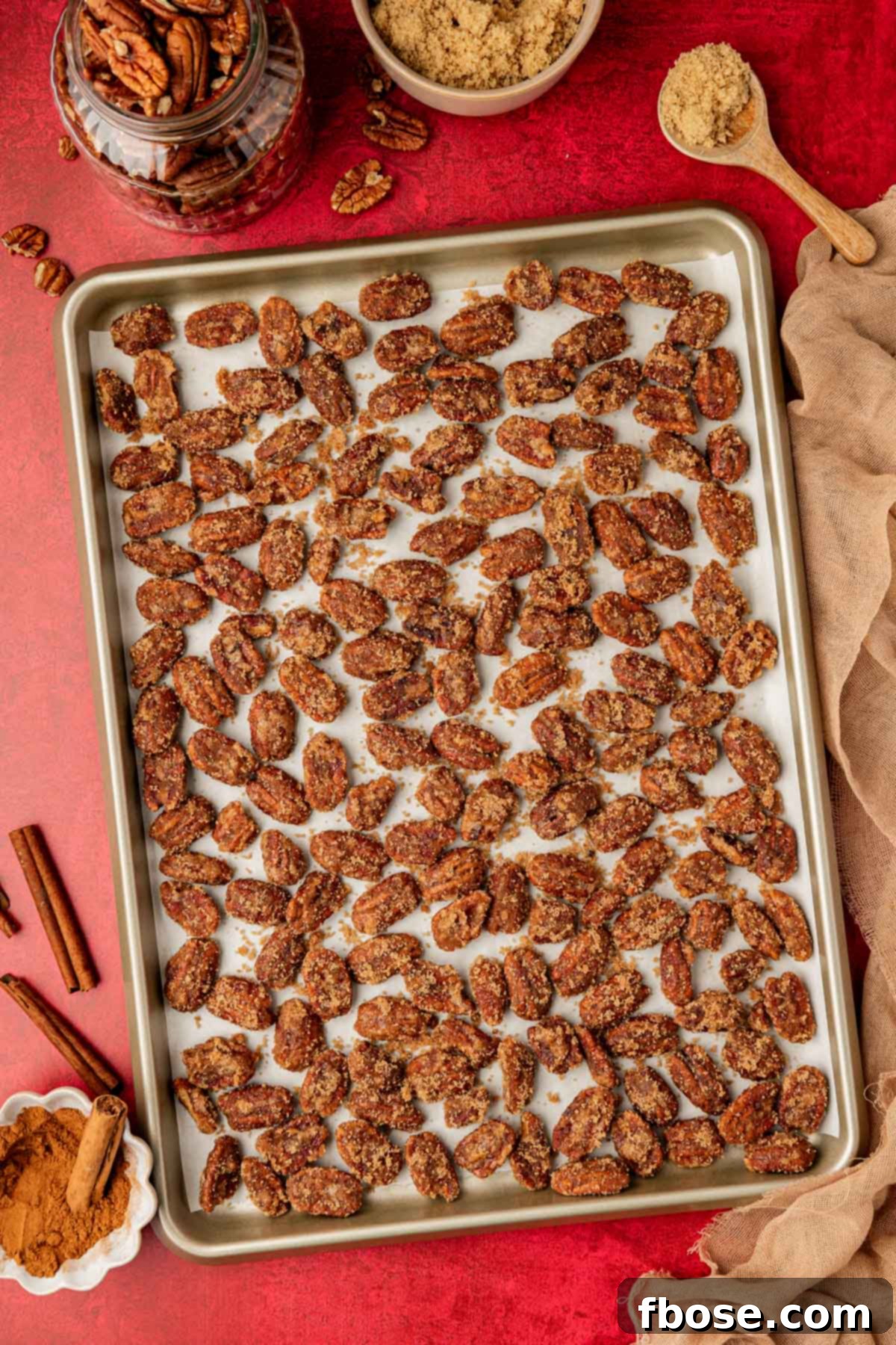 An overhead view of a sheet pan filled with perfectly spaced, golden-brown candied pecans, cooling on parchment paper after cooking.