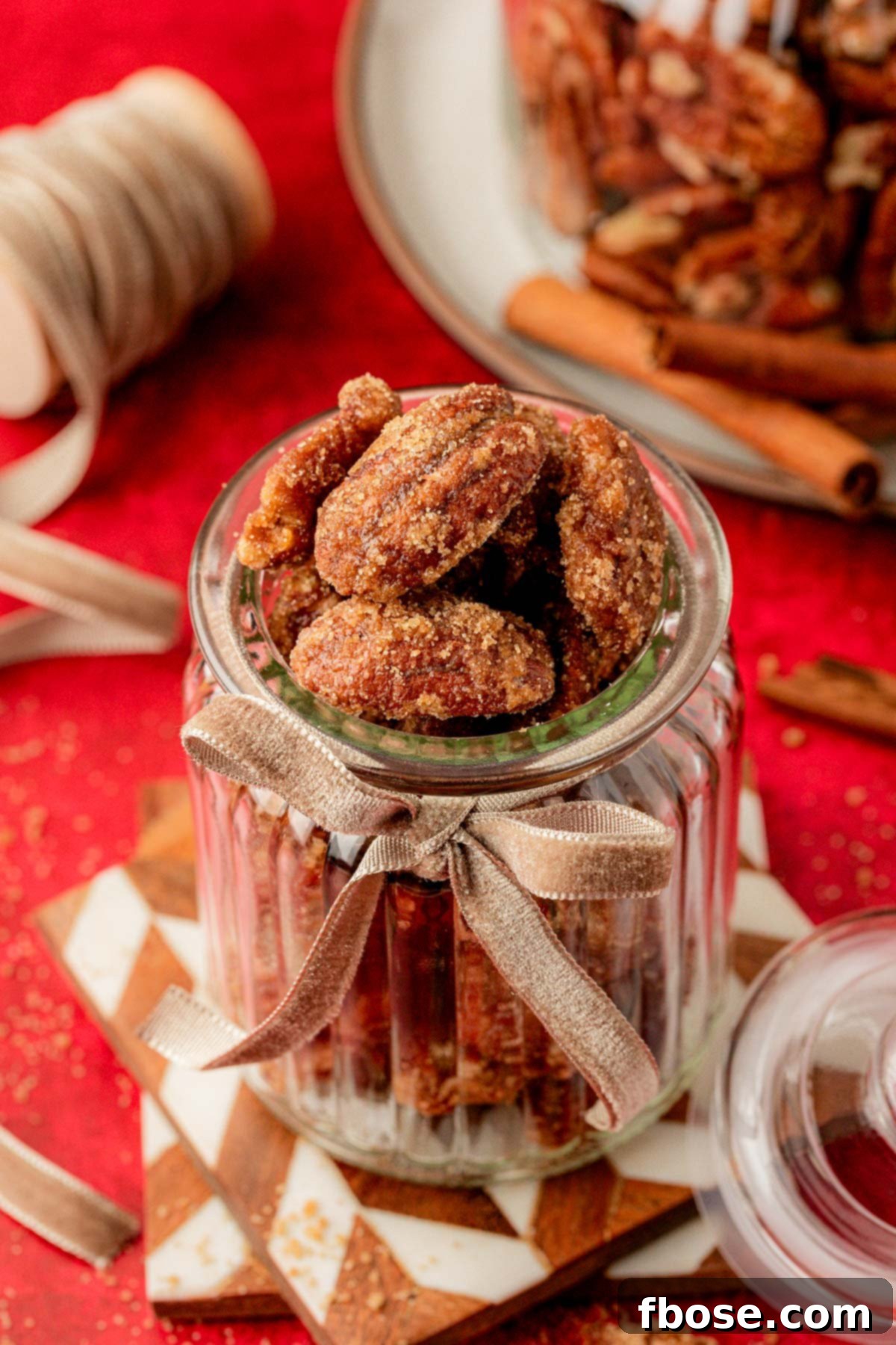 Candied Pecans artfully arranged in a clear glass jar, resting on stacked coasters, ready for gifting or storage.
