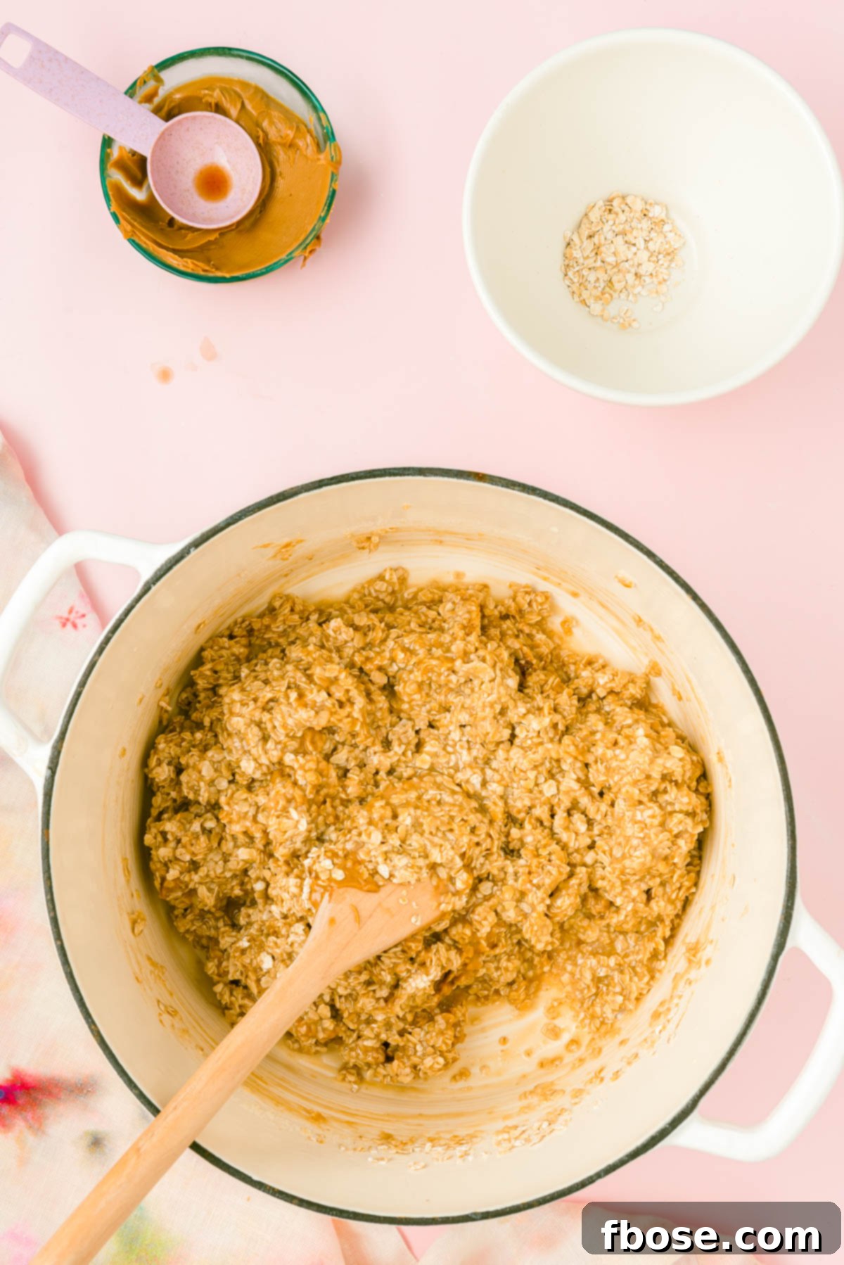 A wooden spoon swiftly mixes oatmeal, creamy cookie butter, and fragrant vanilla extract into the hot butter, milk, and sugar mixture.