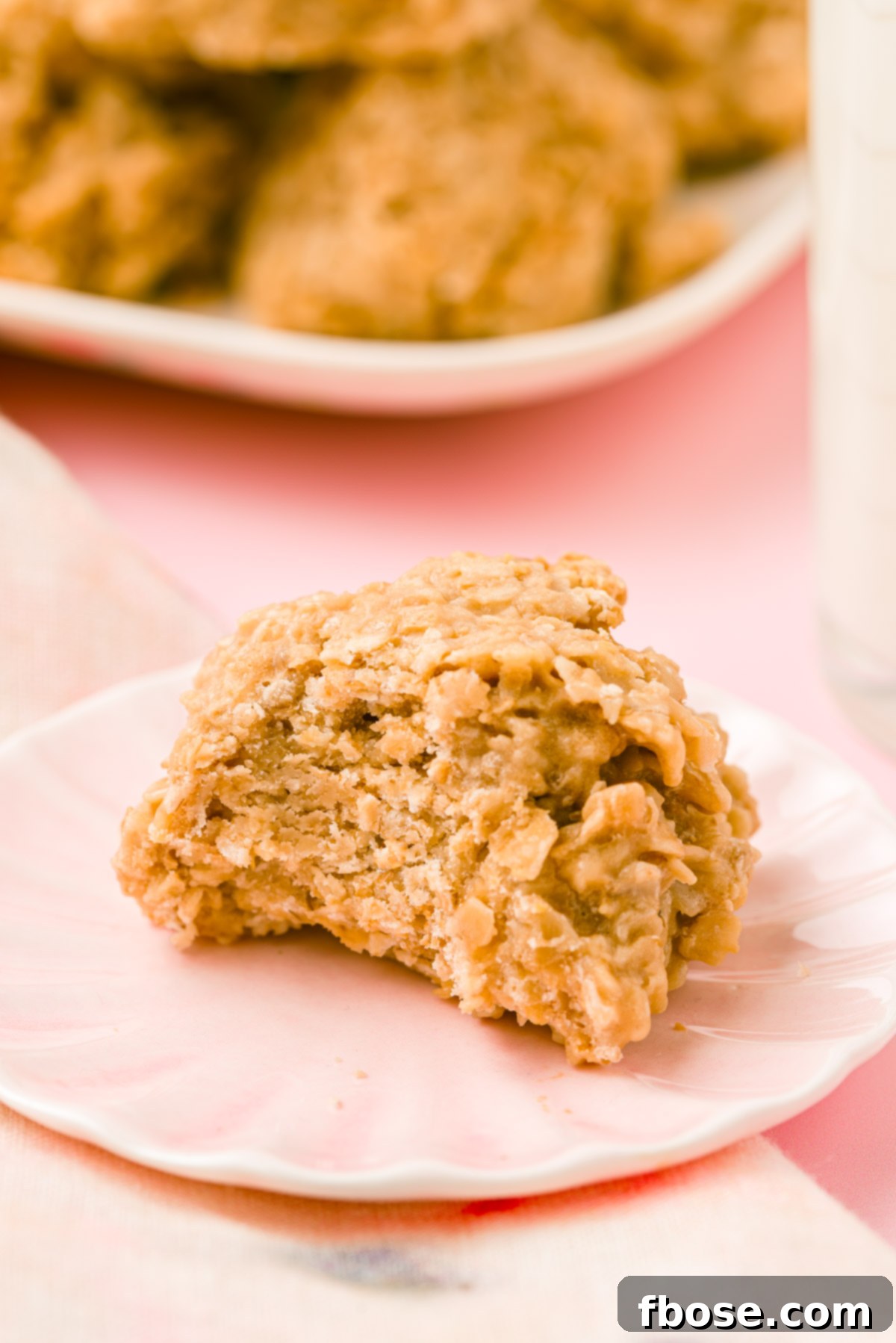 A delectable cookie butter no bake cookie on a pink plate, showing a bite taken out to reveal its chewy, oat-filled interior.