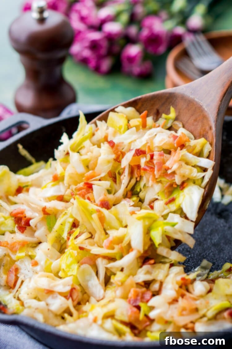 A wooden spoon scooping fried cabbage out of a skillet.