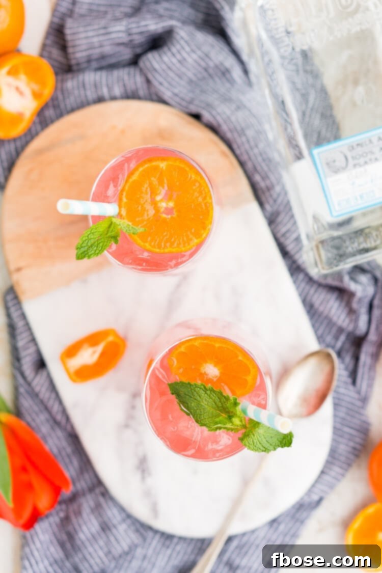 A close-up of the Cactus Cooler Tequila Cocktail with a straw, garnished with tangerine and mint.